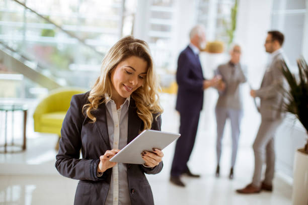 Portrait of young businesswoman using with tablet in office while other business people talking in background